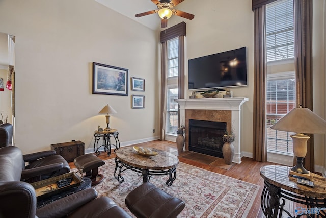 living area with ceiling fan, a tile fireplace, wood finished floors, and baseboards