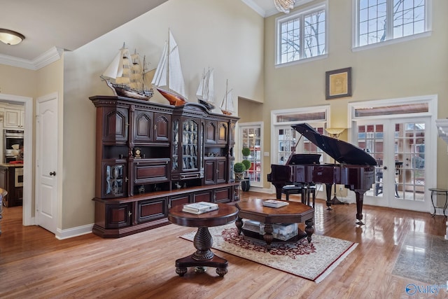 sitting room featuring baseboards, light wood-style flooring, ornamental molding, a high ceiling, and french doors