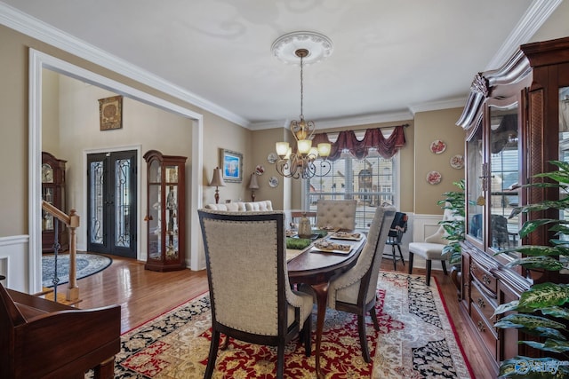 dining area with a chandelier, a decorative wall, wood finished floors, ornamental molding, and wainscoting