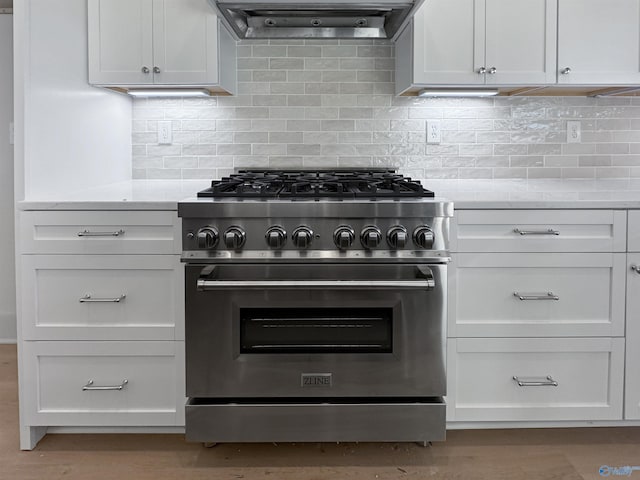 kitchen with tasteful backsplash, range hood, high end stove, and white cabinetry