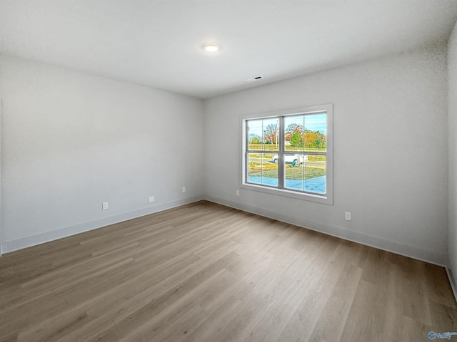 spare room with light wood finished floors, visible vents, and baseboards