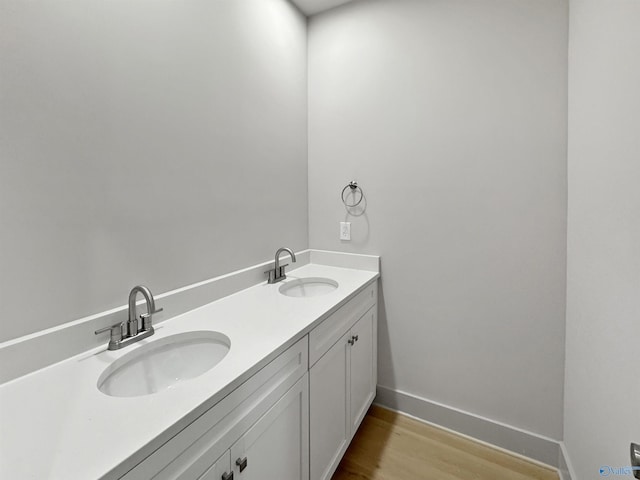 bathroom featuring double vanity, wood finished floors, a sink, and baseboards