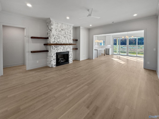 unfurnished living room featuring recessed lighting, ornamental molding, a stone fireplace, light wood-type flooring, and ceiling fan with notable chandelier