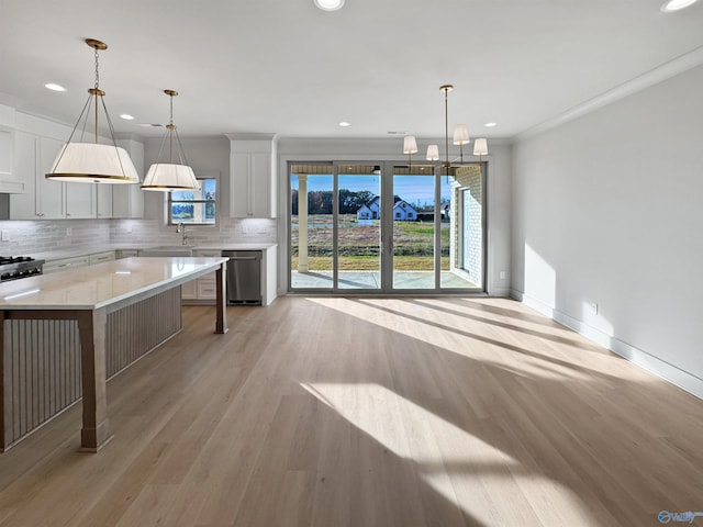 kitchen featuring light countertops, light wood-style flooring, backsplash, stainless steel dishwasher, and baseboards