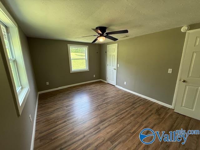 unfurnished bedroom with dark wood-type flooring, a ceiling fan, a textured ceiling, and baseboards