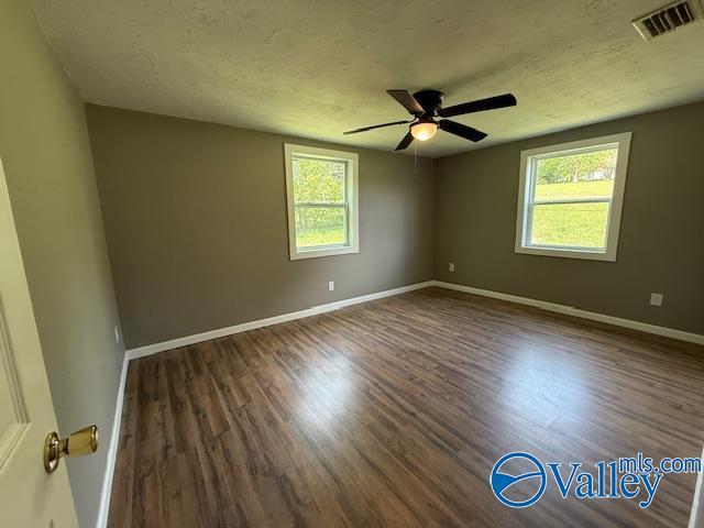 empty room with a ceiling fan, visible vents, wood finished floors, and baseboards