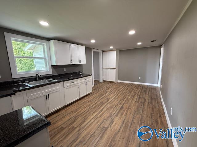kitchen with wood finished floors, white cabinets, a sink, baseboards, and visible vents