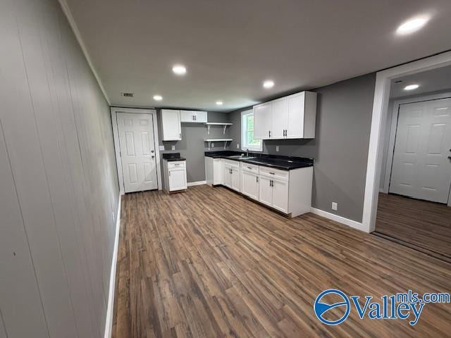 kitchen featuring dark wood finished floors, white cabinets, dark countertops, a sink, and baseboards