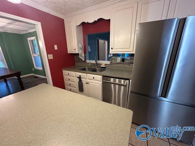 kitchen featuring white cabinetry, crown molding, decorative backsplash, stainless steel appliances, and a sink
