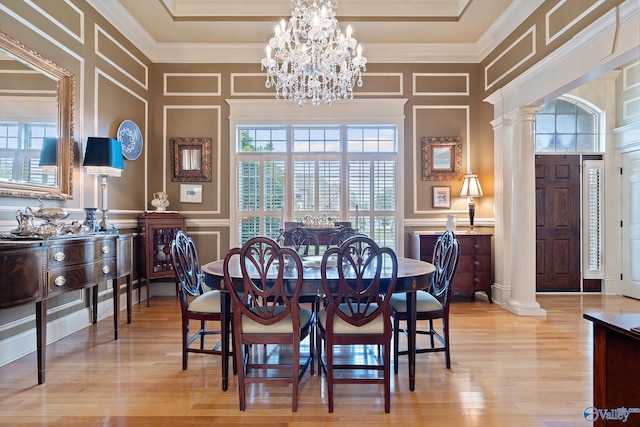 dining room with a notable chandelier, a decorative wall, ornamental molding, ornate columns, and light wood-style flooring