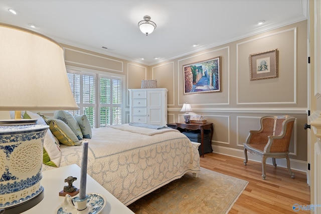 bedroom featuring light wood-style flooring, a decorative wall, ornamental molding, and visible vents