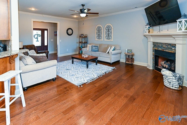 living area featuring a ceiling fan, wood finished floors, crown molding, and a fireplace