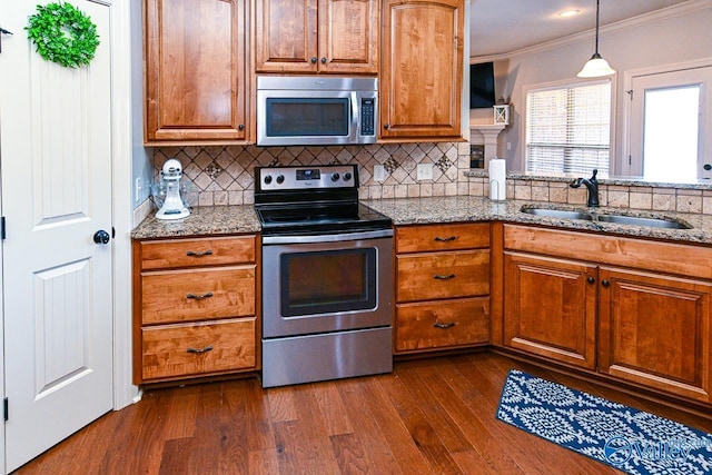 kitchen with light stone countertops, dark wood finished floors, ornamental molding, a sink, and appliances with stainless steel finishes