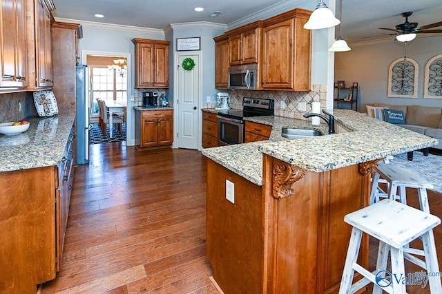 kitchen with brown cabinets, a ceiling fan, a sink, appliances with stainless steel finishes, and a peninsula