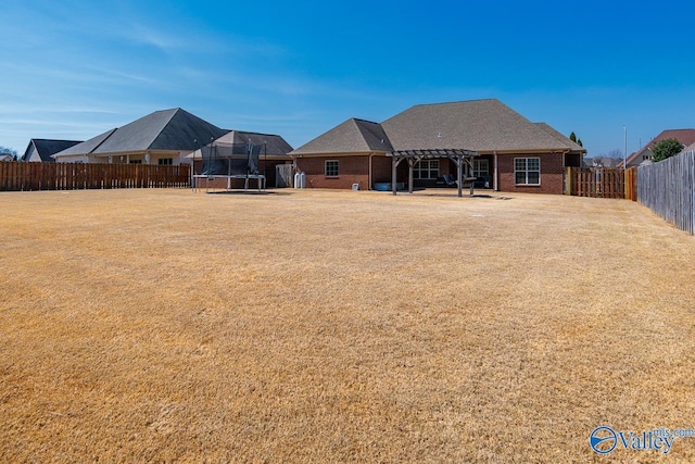 back of property with a fenced backyard, a pergola, a trampoline, a lawn, and brick siding