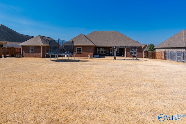 rear view of property featuring a lawn, a pergola, a trampoline, a fenced backyard, and brick siding