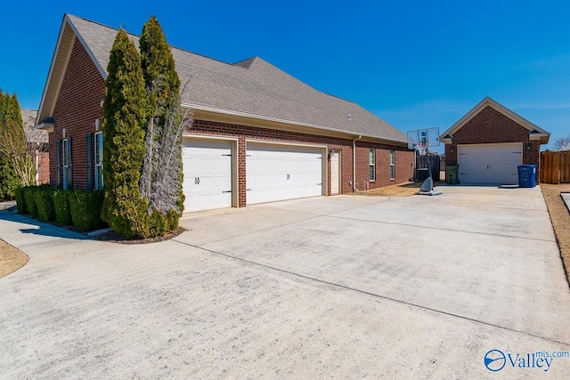 view of home's exterior featuring brick siding, a shingled roof, fence, a garage, and driveway