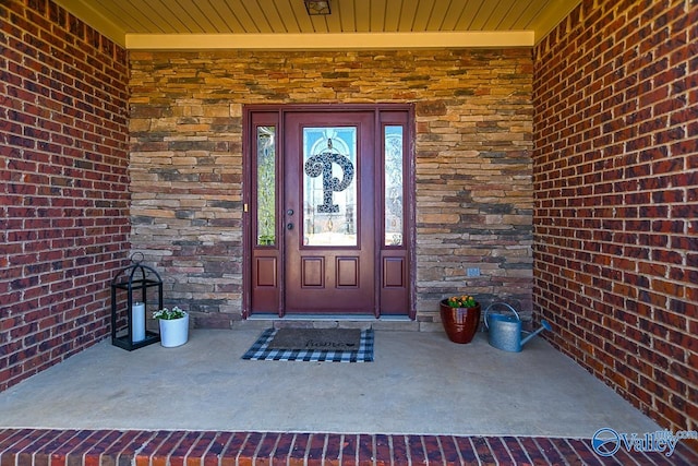 view of exterior entry with a porch, brick siding, and stone siding