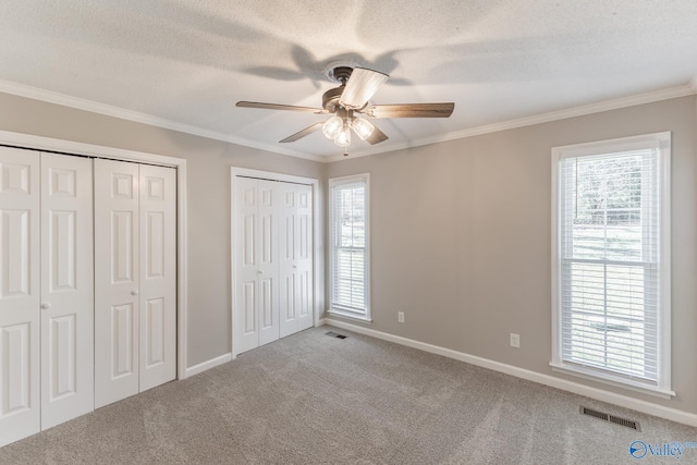 unfurnished bedroom featuring carpet flooring, visible vents, multiple windows, two closets, and crown molding