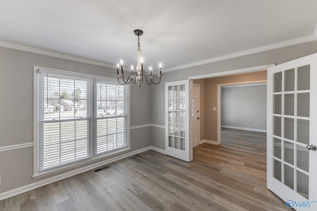 unfurnished room with crown molding, visible vents, an inviting chandelier, wood finished floors, and baseboards