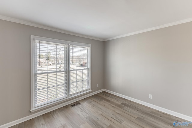 empty room with light wood-style floors, visible vents, ornamental molding, and baseboards