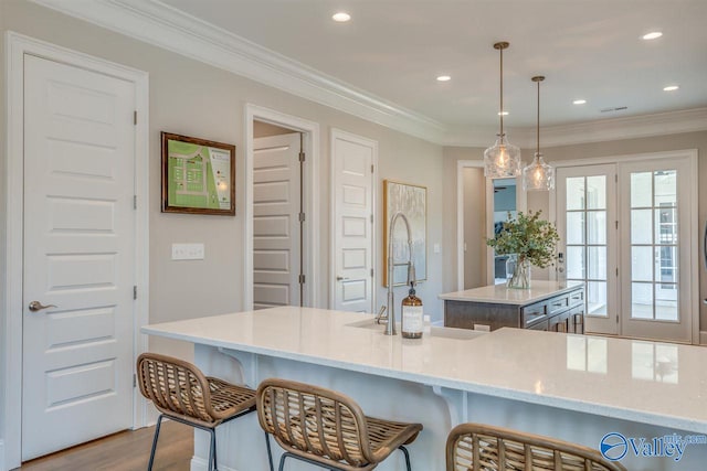 kitchen featuring a kitchen island with sink, light hardwood / wood-style flooring, crown molding, light stone countertops, and decorative light fixtures