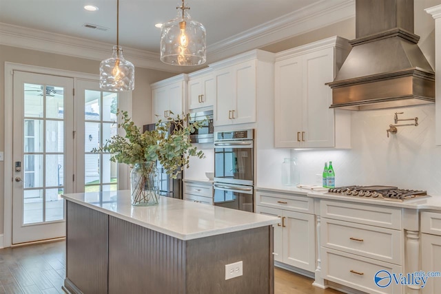 kitchen featuring appliances with stainless steel finishes, light hardwood / wood-style floors, pendant lighting, white cabinets, and decorative backsplash