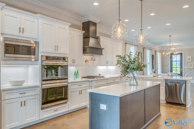 kitchen featuring premium range hood, appliances with stainless steel finishes, hanging light fixtures, and white cabinetry