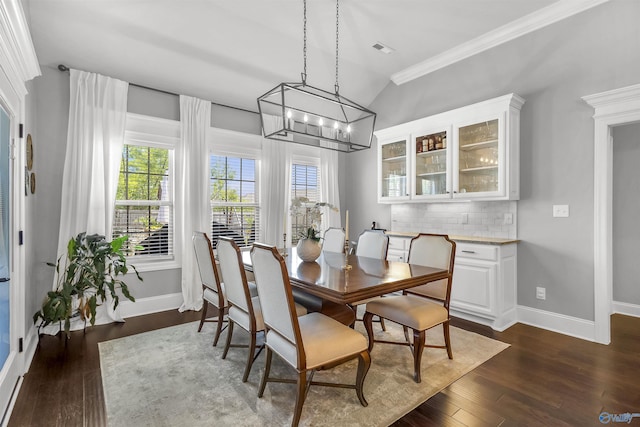 dining room with baseboards, dark wood-style floors, a notable chandelier, ornamental molding, and lofted ceiling