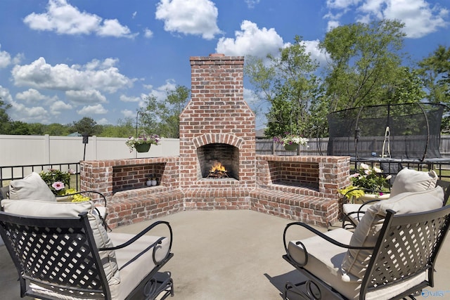 view of patio / terrace with a fenced backyard, a trampoline, and an outdoor brick fireplace