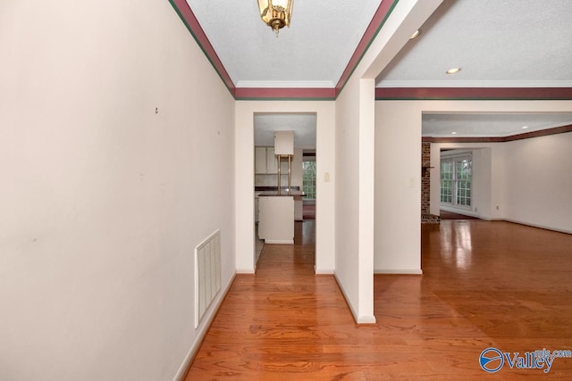 corridor featuring wood-type flooring, a textured ceiling, and ornamental molding