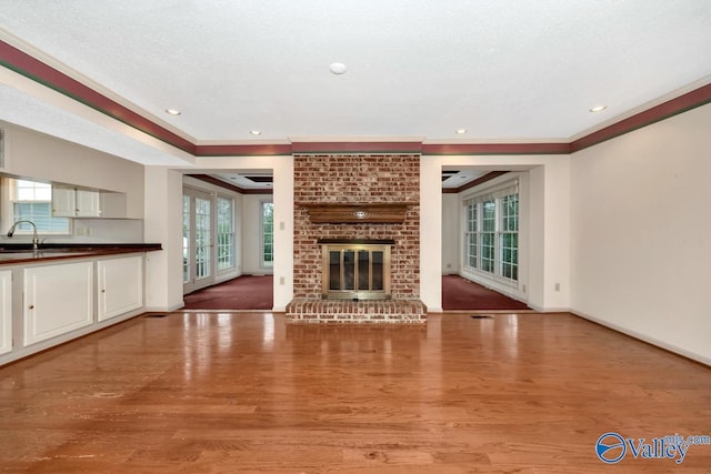 unfurnished living room with ornamental molding, hardwood / wood-style floors, a healthy amount of sunlight, and a brick fireplace