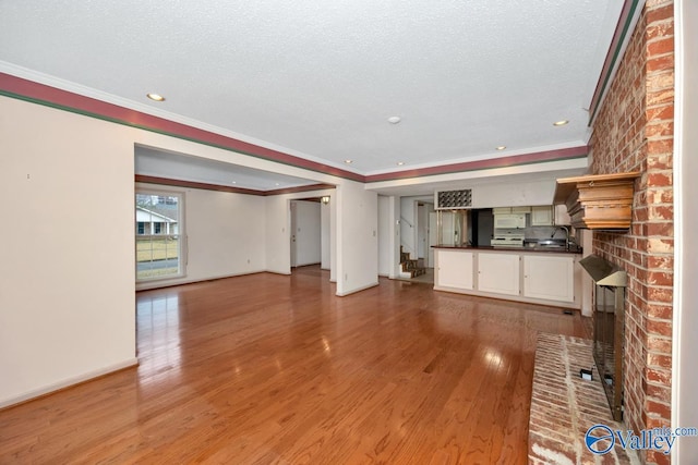 unfurnished living room featuring crown molding, a fireplace, light hardwood / wood-style floors, and a textured ceiling