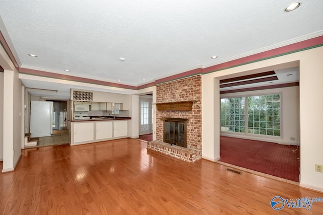 unfurnished living room with a raised ceiling, crown molding, light hardwood / wood-style floors, and a brick fireplace