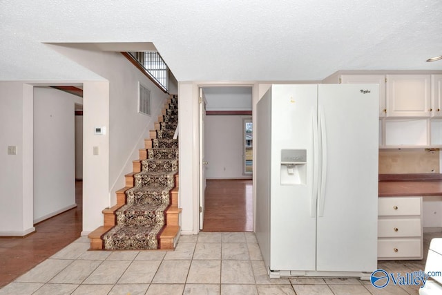 kitchen with white fridge with ice dispenser, white cabinets, light hardwood / wood-style floors, and a textured ceiling