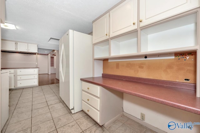 kitchen featuring light tile patterned floors, a textured ceiling, white fridge, and white cabinetry