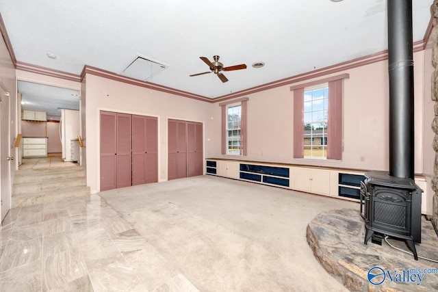 living room with ceiling fan, a wood stove, and ornamental molding