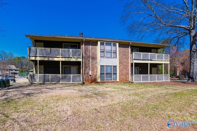 back of house featuring a balcony, a lawn, and brick siding