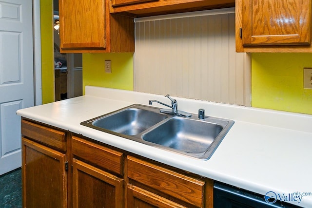kitchen with light countertops, a sink, brown cabinetry, and black dishwasher