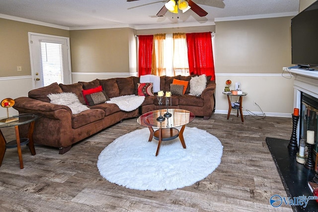 living room with a glass covered fireplace, wood finished floors, ornamental molding, and a ceiling fan