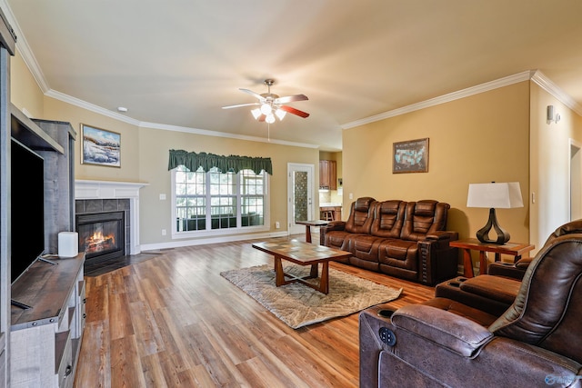 living room with a tiled fireplace, crown molding, wood-type flooring, and ceiling fan