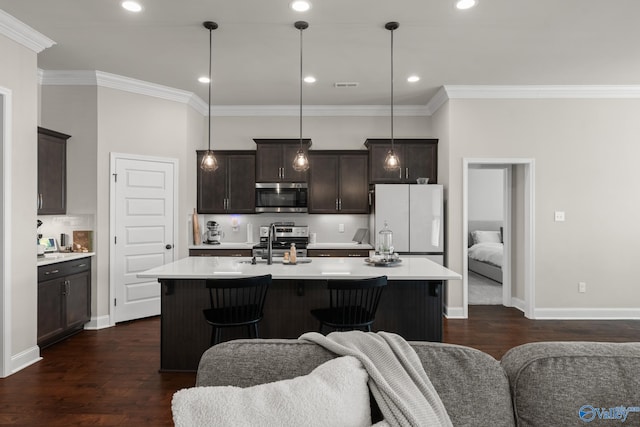 kitchen featuring dark hardwood / wood-style flooring, pendant lighting, a center island with sink, appliances with stainless steel finishes, and ornamental molding