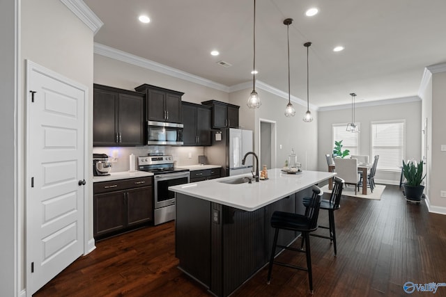 kitchen with stainless steel appliances, dark wood-type flooring, sink, decorative light fixtures, and an island with sink