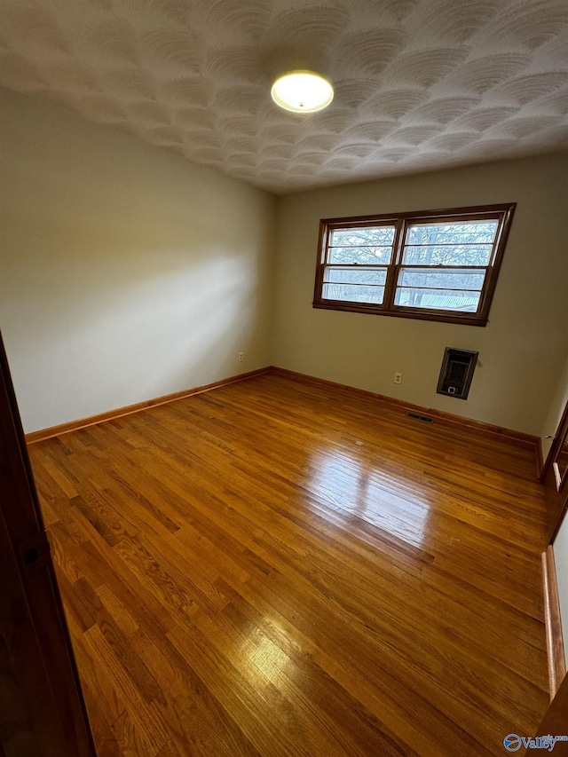 unfurnished room featuring wood-type flooring, heating unit, and a textured ceiling