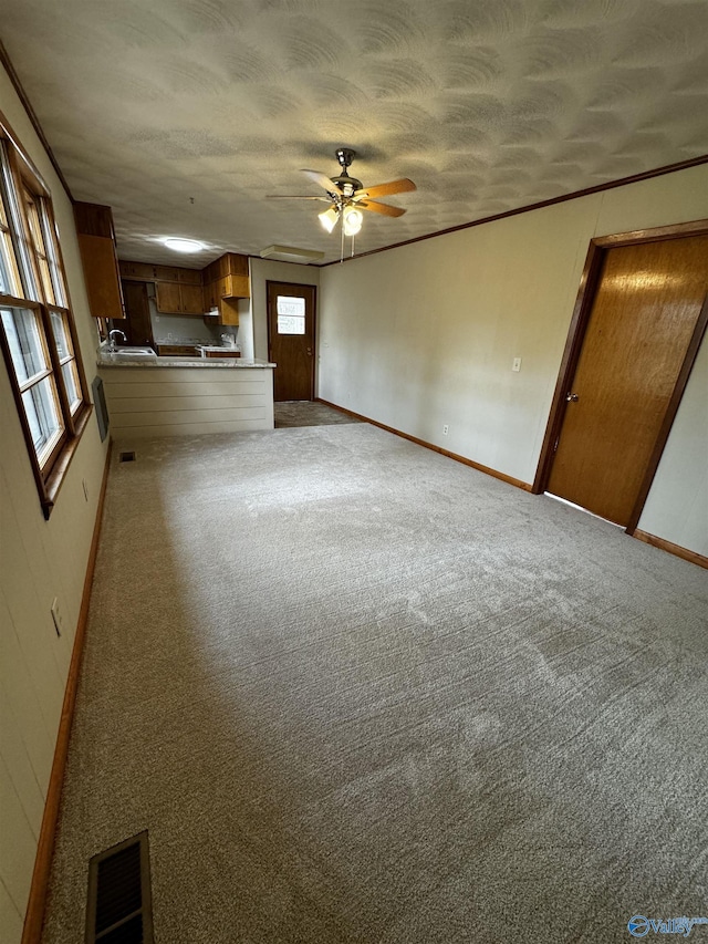 unfurnished living room featuring ornamental molding, light colored carpet, a textured ceiling, and ceiling fan