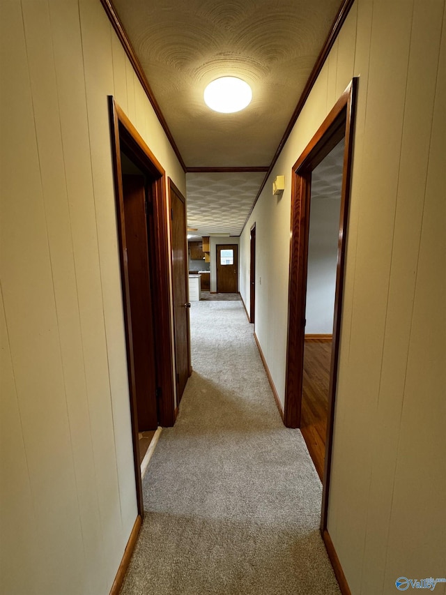 hall featuring ornamental molding, a textured ceiling, light carpet, and wood walls