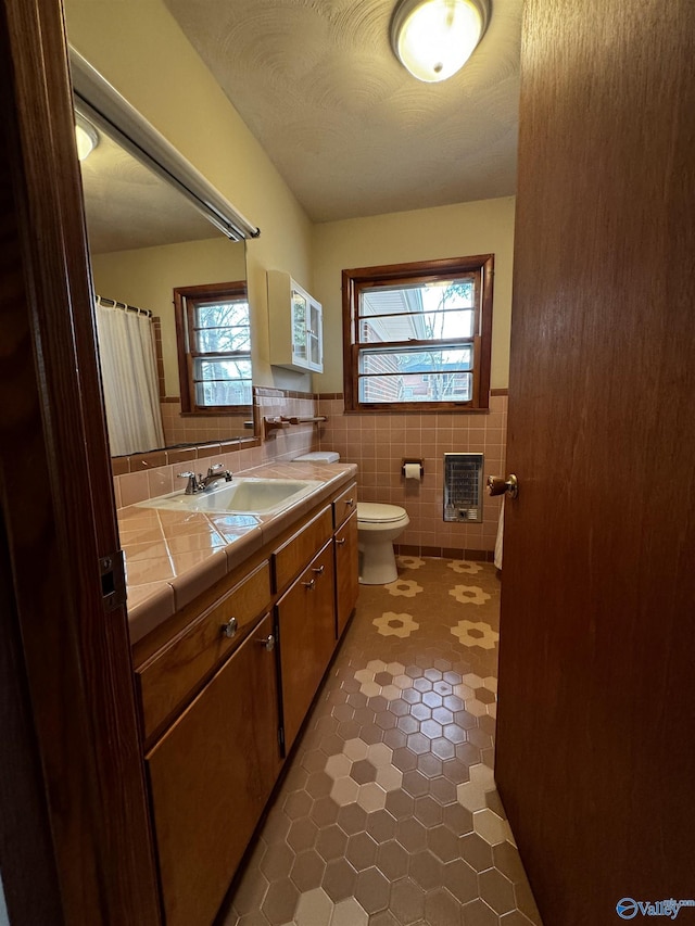 bathroom featuring vanity, heating unit, tile walls, and toilet