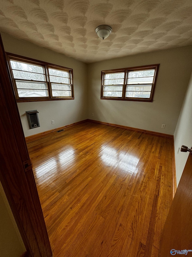 unfurnished room with plenty of natural light, a textured ceiling, heating unit, and light wood-type flooring