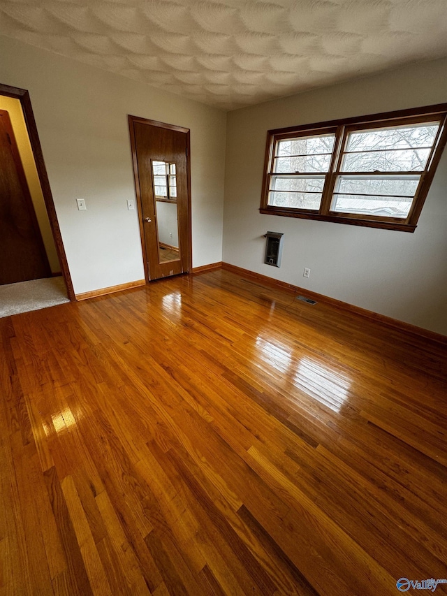 unfurnished room featuring hardwood / wood-style flooring, a healthy amount of sunlight, heating unit, and a textured ceiling