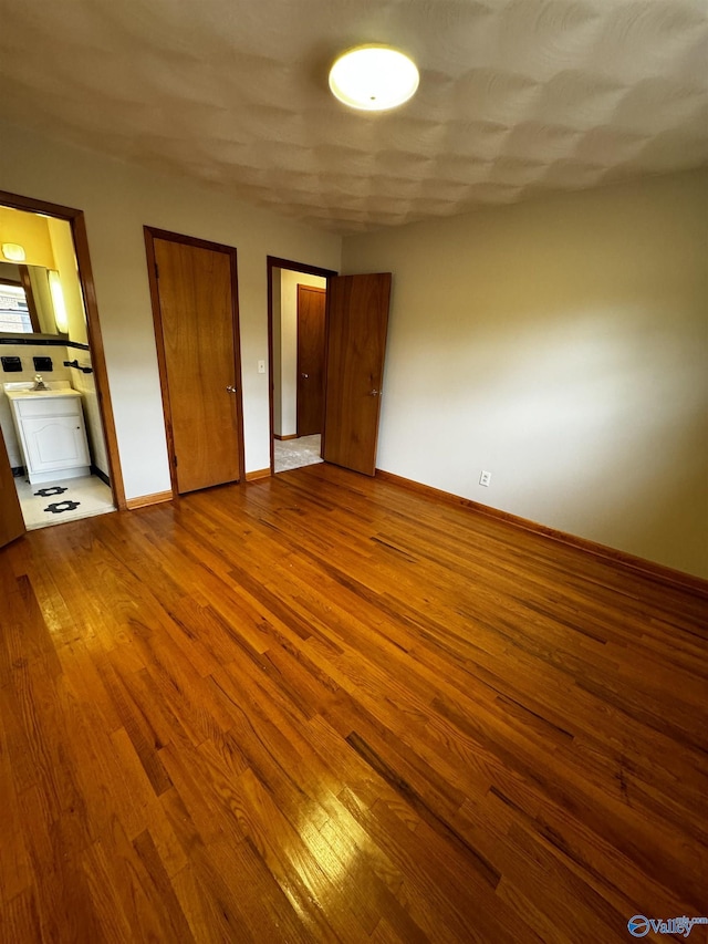 unfurnished bedroom with ensuite bath, wood-type flooring, and two closets